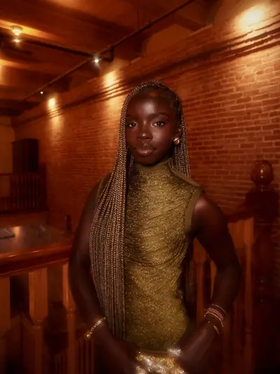 Joy in a gold knit dress against a brick wall