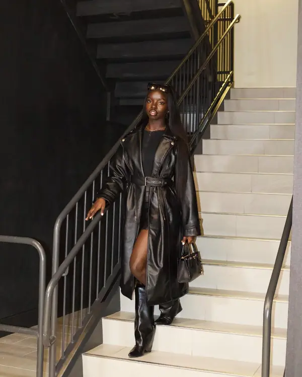 Joy in a black leather trench coat on white stairs